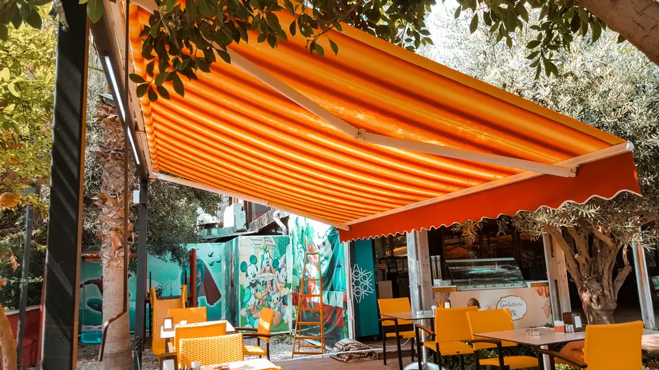 Kafe terasında turuncu çizgili mafsallı tente